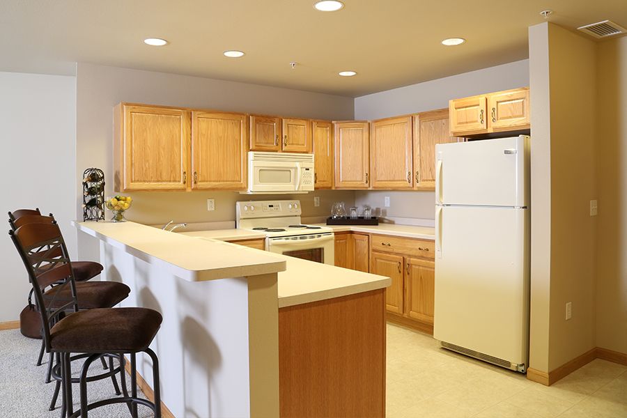A modern kitchen with wooden cabinets and a countertop featuring bar stools and essential appliances.