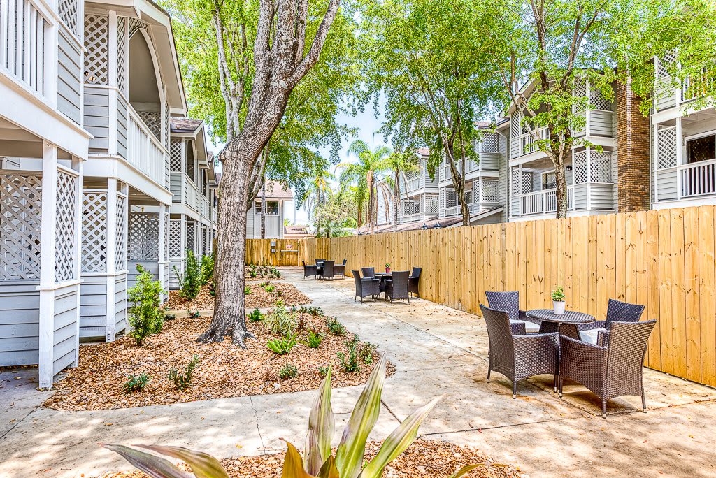 A serene outdoor seating area with tables and chairs surrounded by apartment buildings, trees, and a wooden fence.
