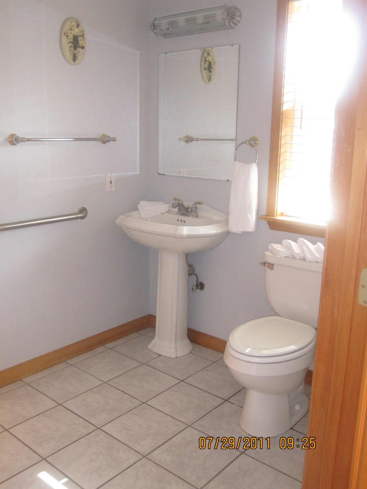 A small bathroom with a pedestal sink, toilet, mirror, and towel rack.