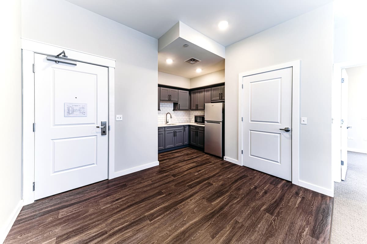 A modern apartment interior featuring a compact kitchen with sleek finishes and wood flooring.