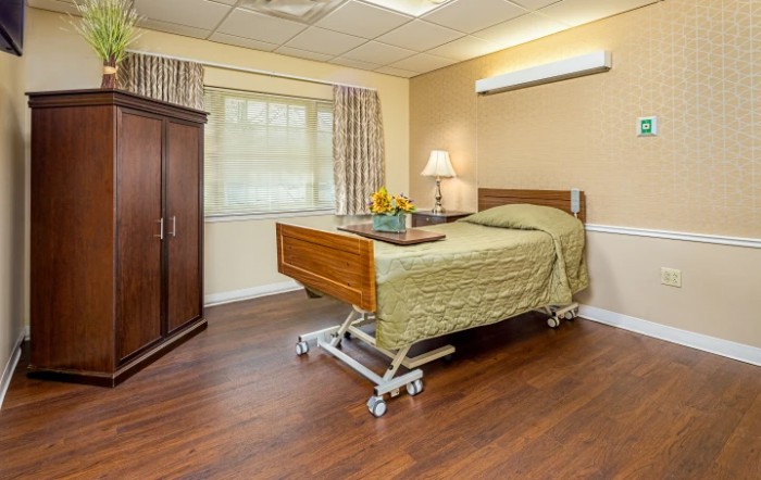 A well-furnished hospital room with a bed, wardrobe, and window.