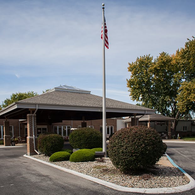 A building with a flagpole and landscaped driveway under a cloudy sky.