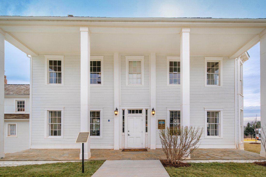 A two-story white building with columns and large windows.