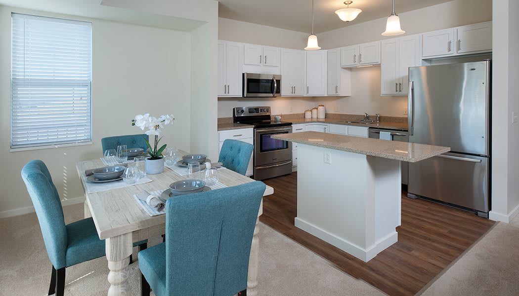 A modern kitchen and dining area featuring white cabinetry, a kitchen island, and elegant dining table with blue chairs.