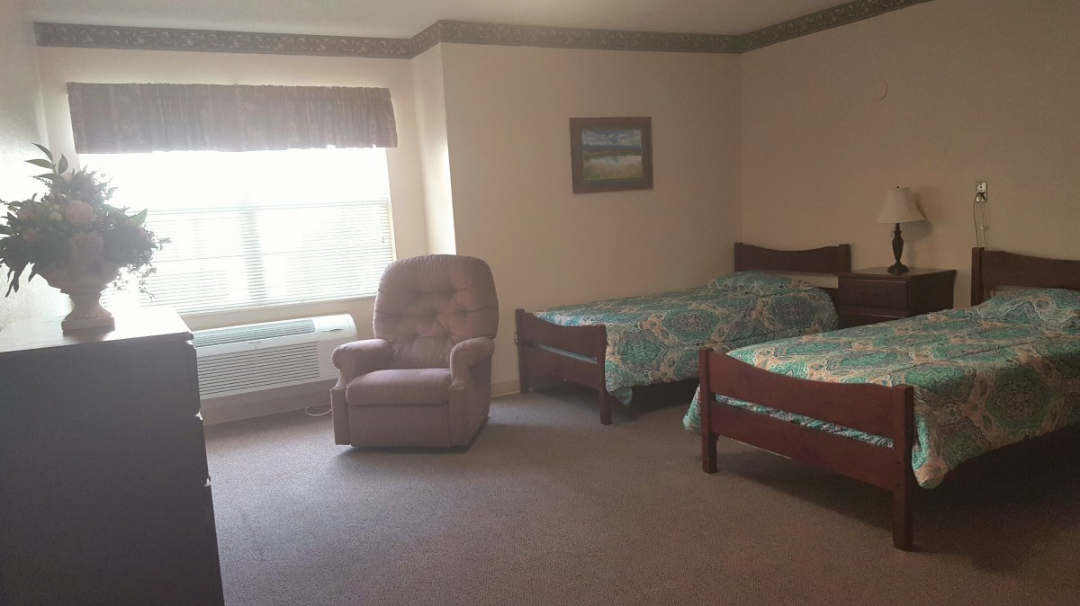 A cozy bedroom with two beds, a recliner chair, and a large window.