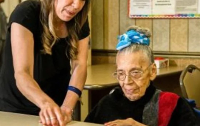 A young woman assists an elderly woman indoors.