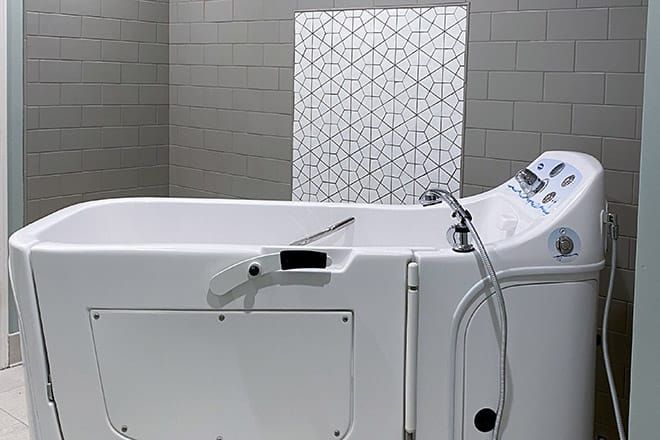 A modern white bathtub with a shower head in a stylish bathroom setting.