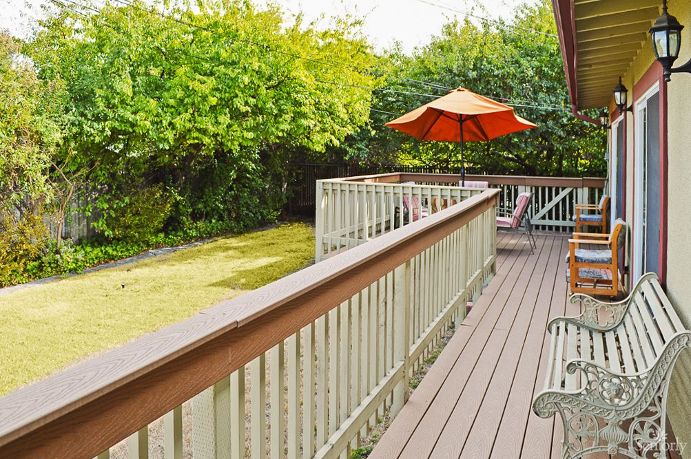 A spacious backyard featuring a wooden deck with outdoor furniture and an umbrella, surrounded by lush greenery.