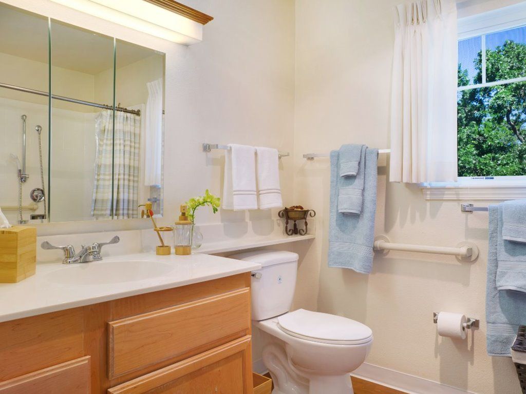A clean and bright bathroom featuring a mirror, toilet, and sink with wooden cabinetry.