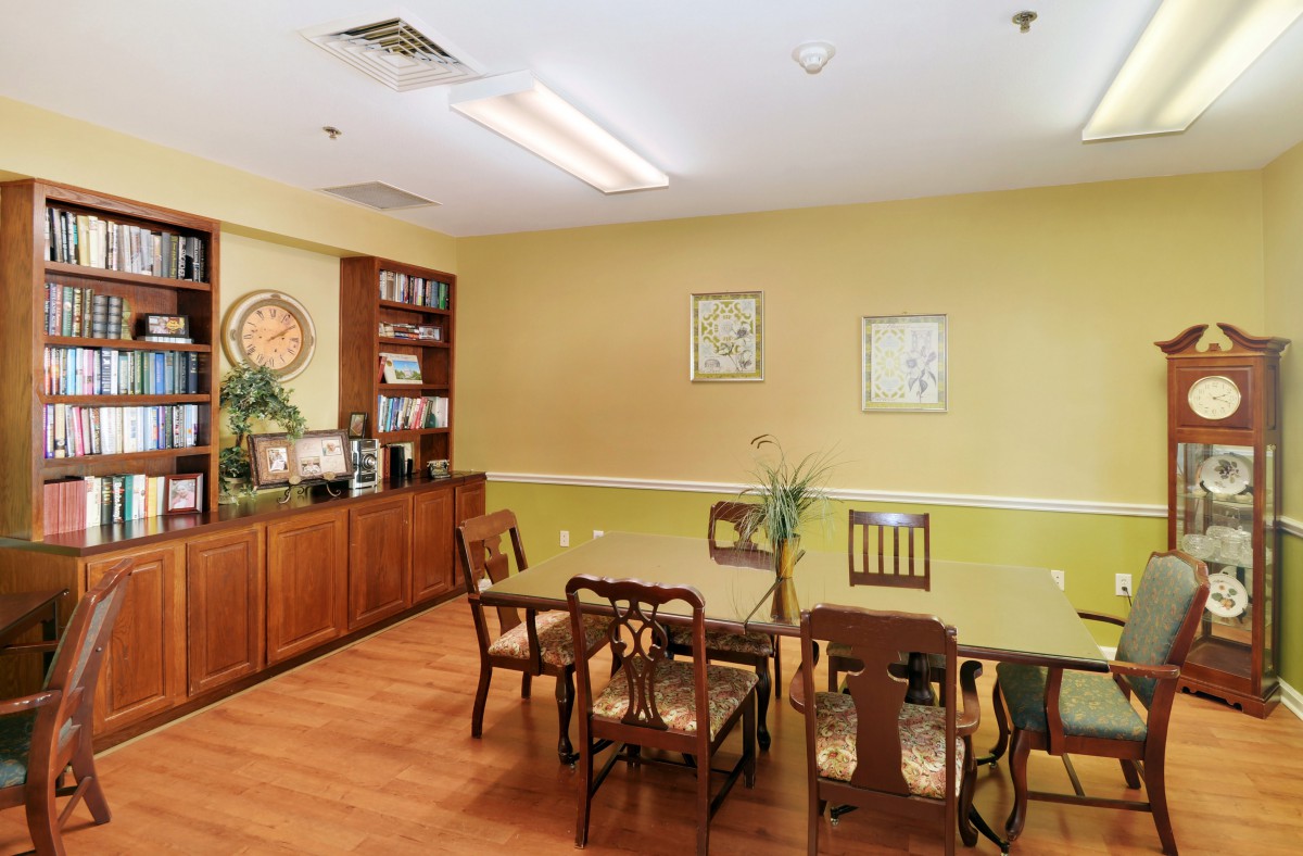 A cozy dining area with wooden chairs and table, decorated with wall art and a bookshelf in the corner.