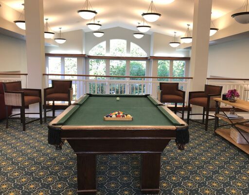 A well-lit game room featuring a billiards table surrounded by chairs.
