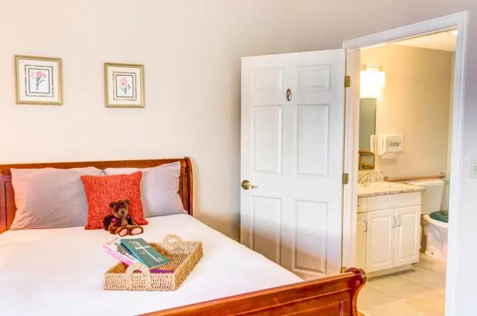 A cozy bedroom with an adjacent bathroom, featuring a bed with colorful pillows and a tray on top.