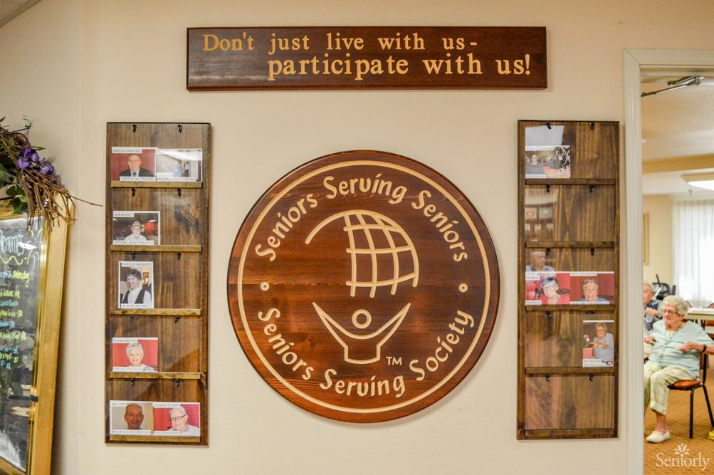 A community center sign encourages participation with the phrase 'Don't just live with us, participate with us!' alongside a logo for Seniors Serving Seniors.