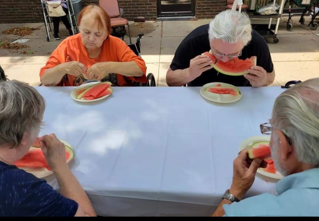 Seniors enjoying a watermelon gathering outdoors.