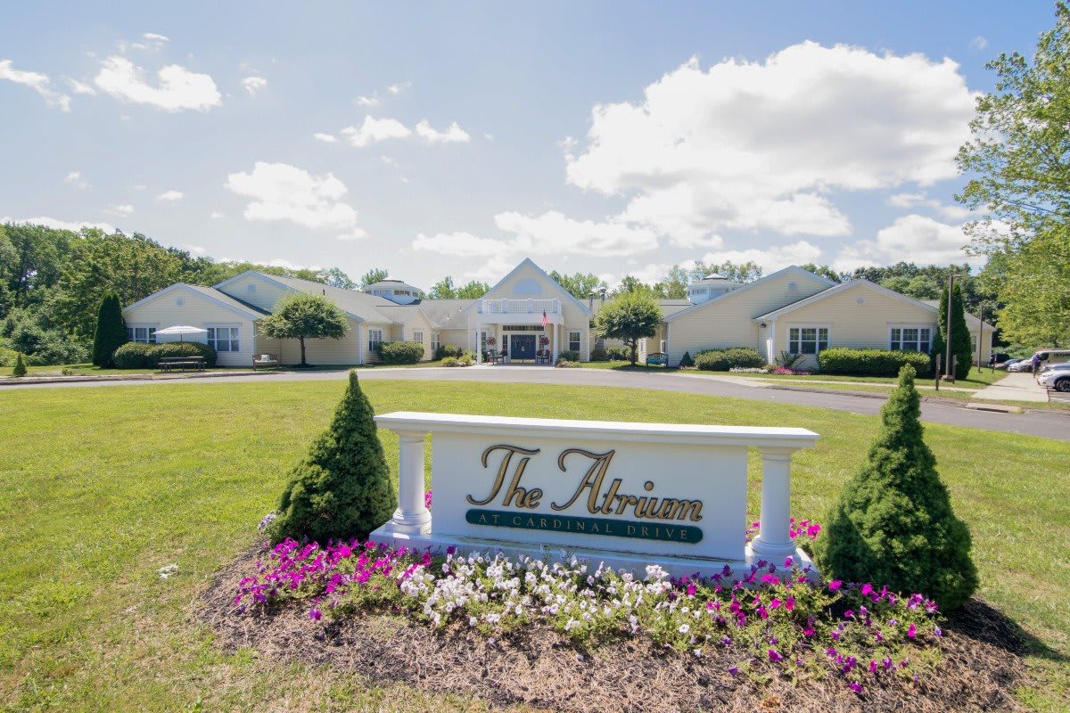 A landscaped area with a sign reading 'The Atrium' in front of a large building complex under a partly cloudy sky.