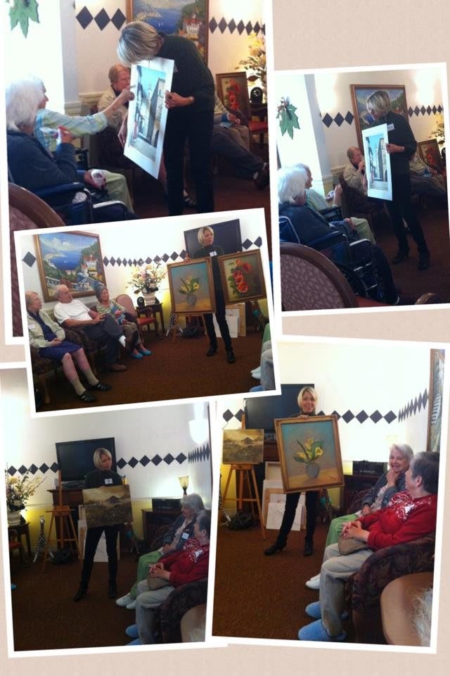 A group of people attending an art presentation, showcasing various paintings in a cozy indoor setting.