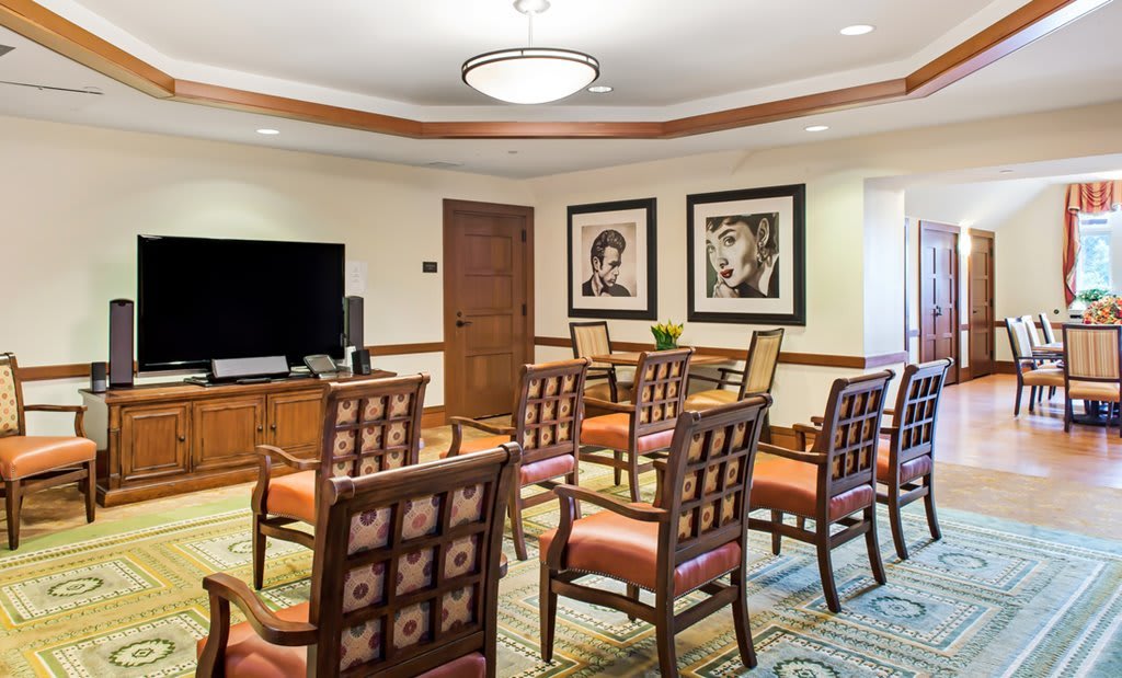 A neatly arranged conference room with chairs facing a TV and framed portraits on the walls.