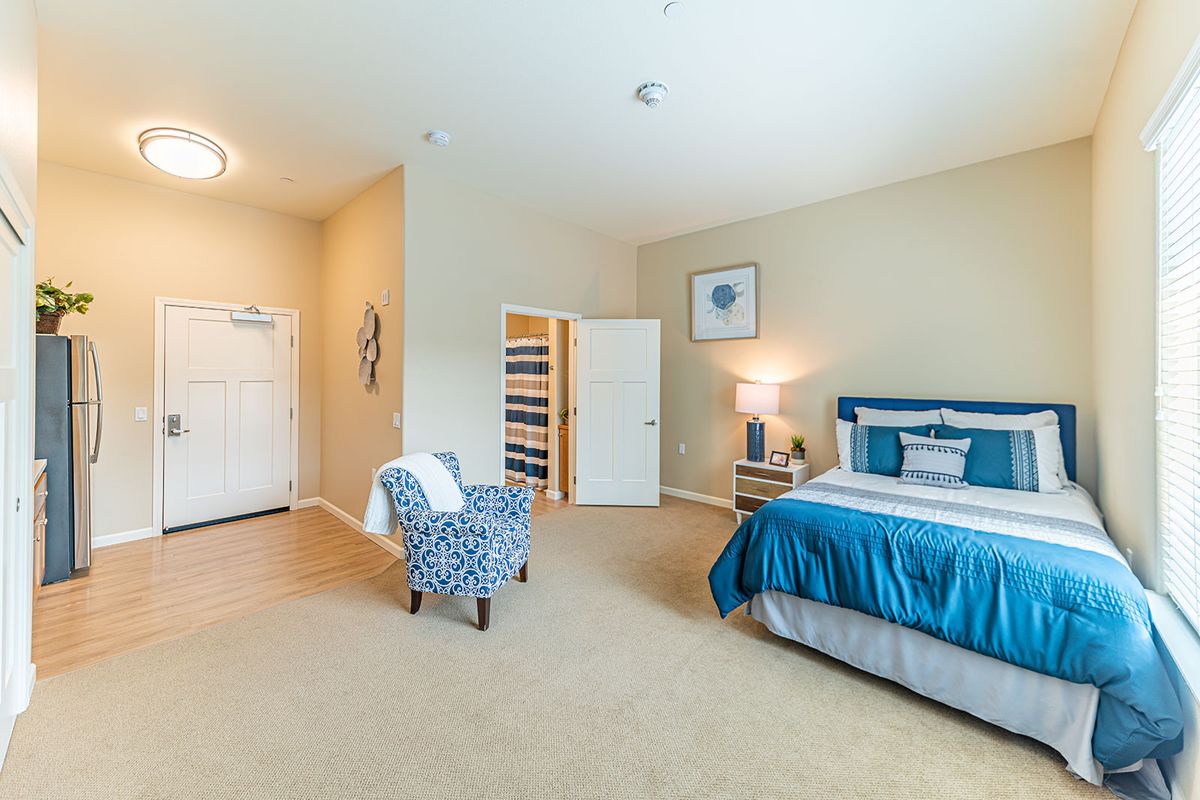 A modern bedroom with a neatly made bed, a patterned armchair, and tasteful decor.
