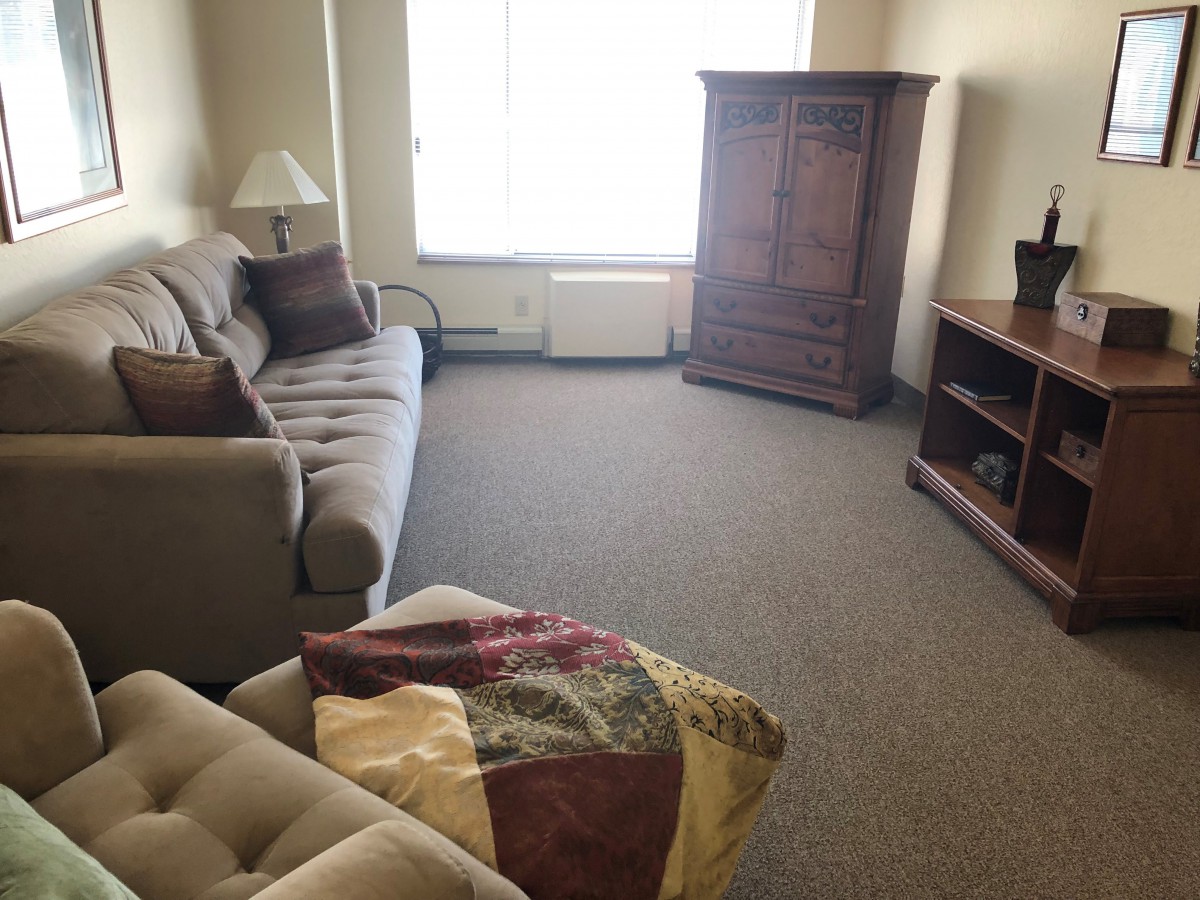 A cozy living room with a sofa, armoire, and television stand.
