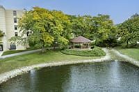 A scenic view of a gazebo by a lake surrounded by lush trees.
