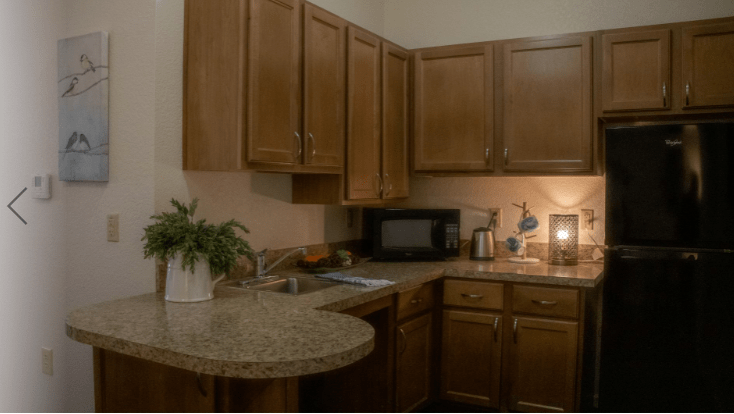 A cozy kitchen with wooden cabinets and a granite countertop featuring a microwave, sink, and small appliances.