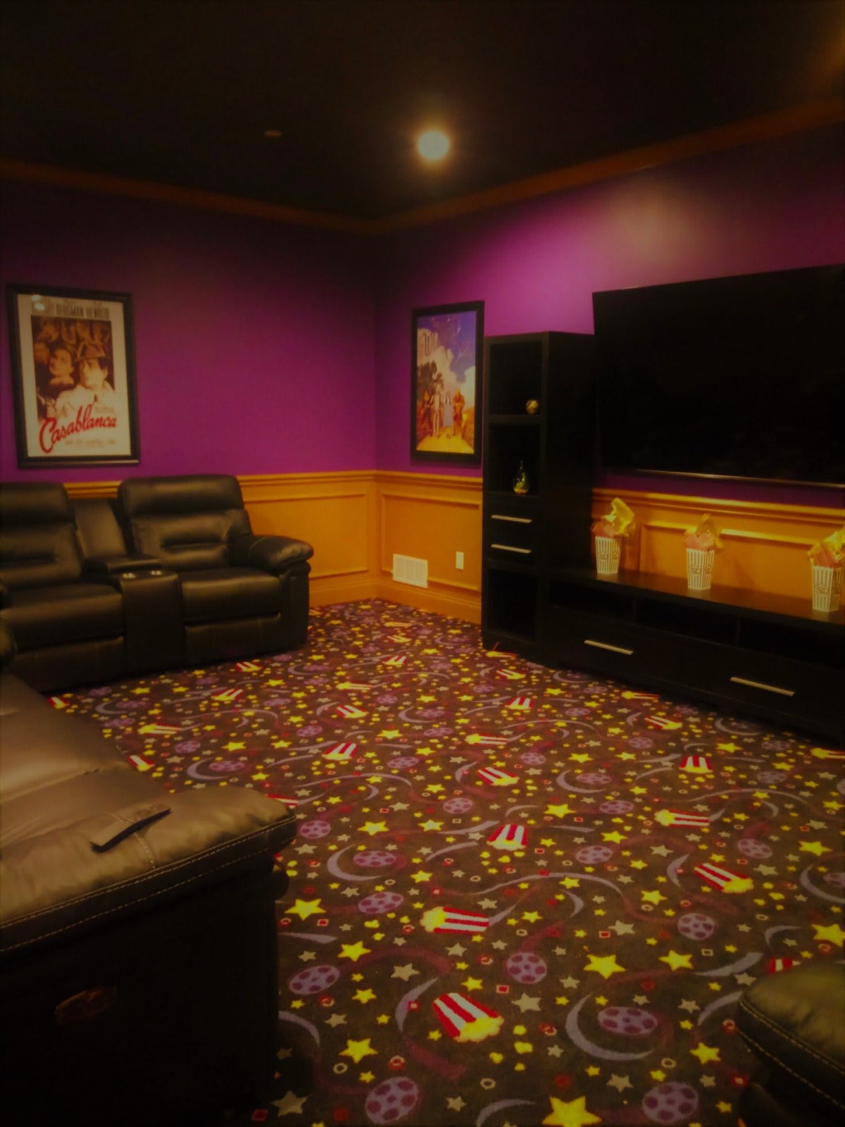A cozy home theater room with purple walls, comfortable leather seating, and decorative carpeting.