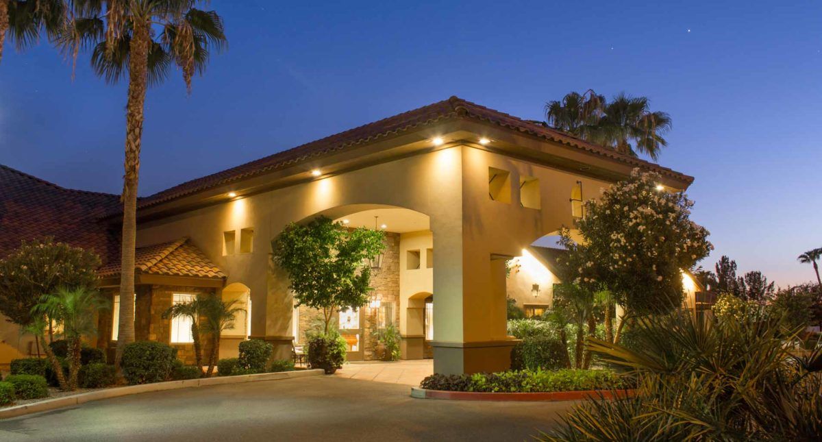 A well-lit building entrance at night, featuring an archway and surrounding greenery.