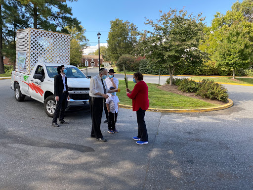 A group of people engaged in conversation near a truck in a green outdoor setting.