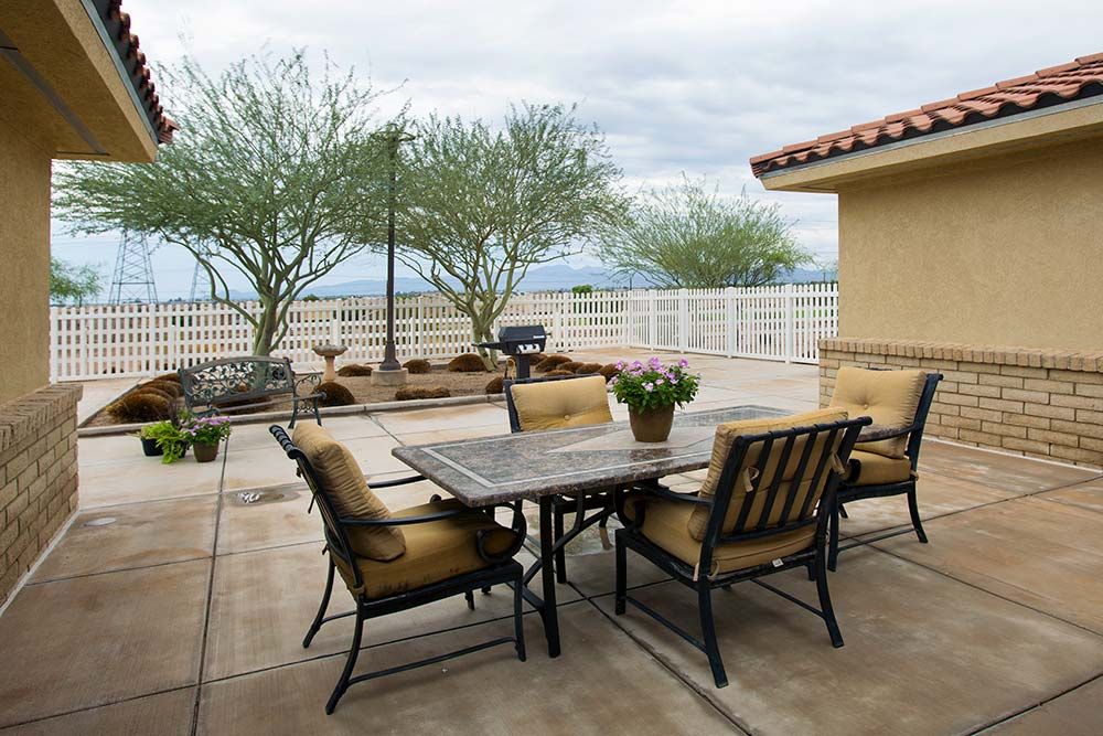 An inviting outdoor patio area with a table and chairs, surrounded by plants and trees under an overcast sky.