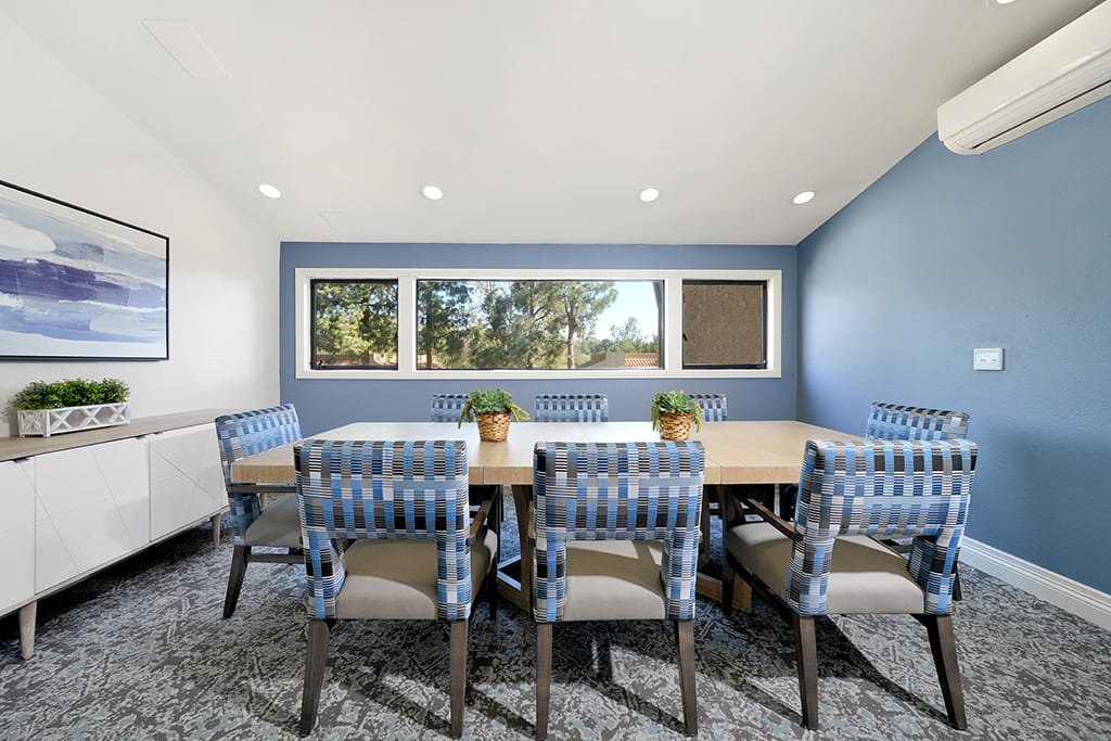 A modern conference room with a long table, surrounded by blue upholstered chairs and featuring large windows.