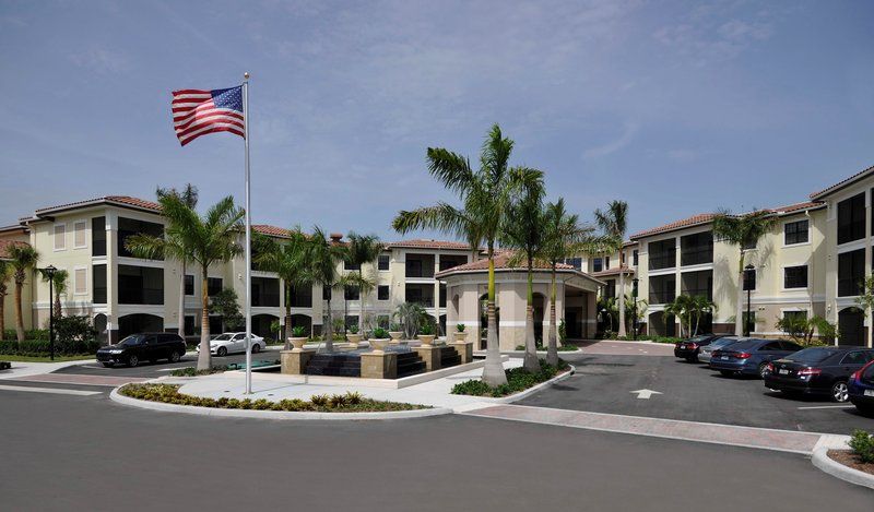 A building entrance surrounded by palm trees with an American flag flying nearby.
