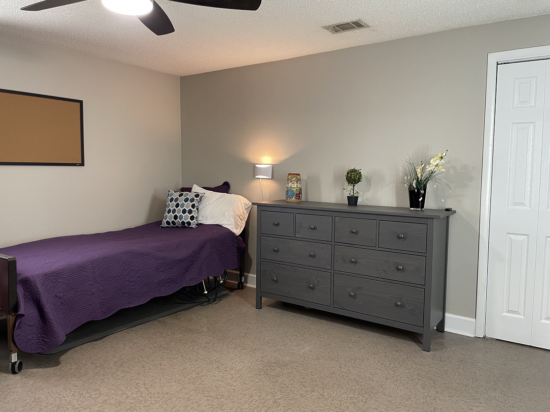 A minimalist bedroom with a single bed, dresser, and soft lighting.