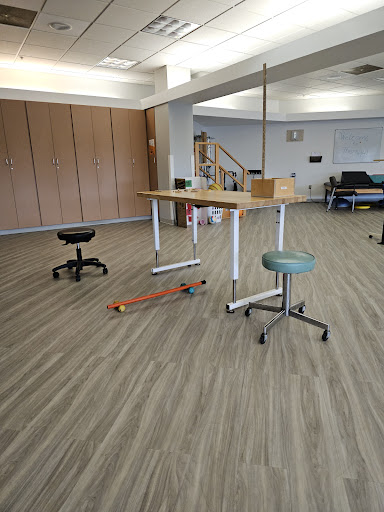 A spacious workplace featuring various types of furniture, including a standing table and rolling chairs.