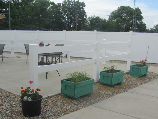 A serene outdoor space featuring a white fence, potted plants, and furniture for relaxing.