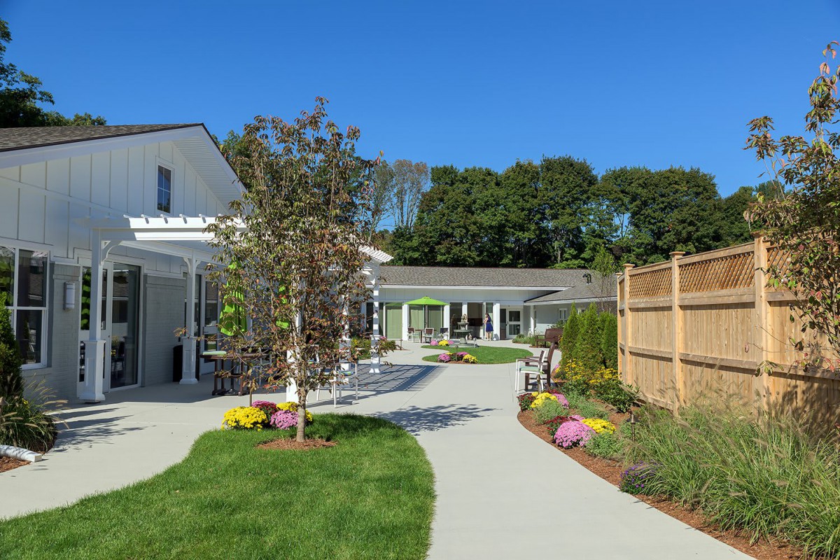 A beautiful garden pathway leading to a house with a wooden fence and vibrant flowers.