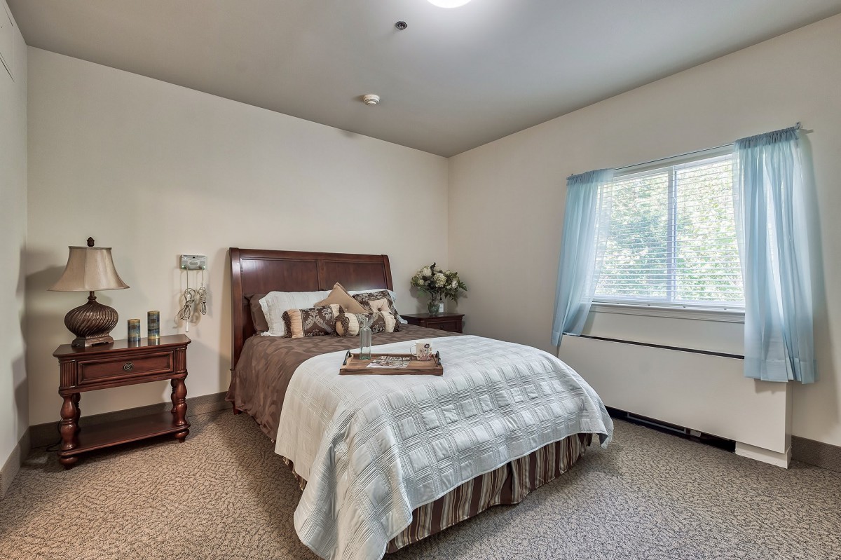 A cozy bedroom with a neatly made bed, featuring decorative pillows and a nightstand with a lamp.