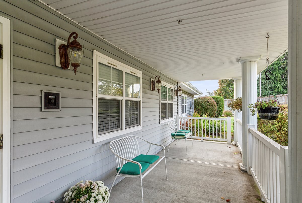 A cozy porch with green-cushioned chairs and potted flowers beside a house.