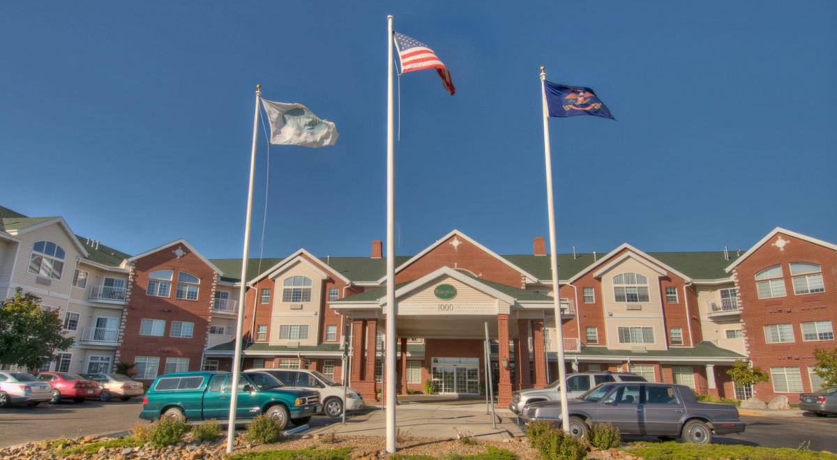A hotel entrance with three flags and parked cars on a clear day.