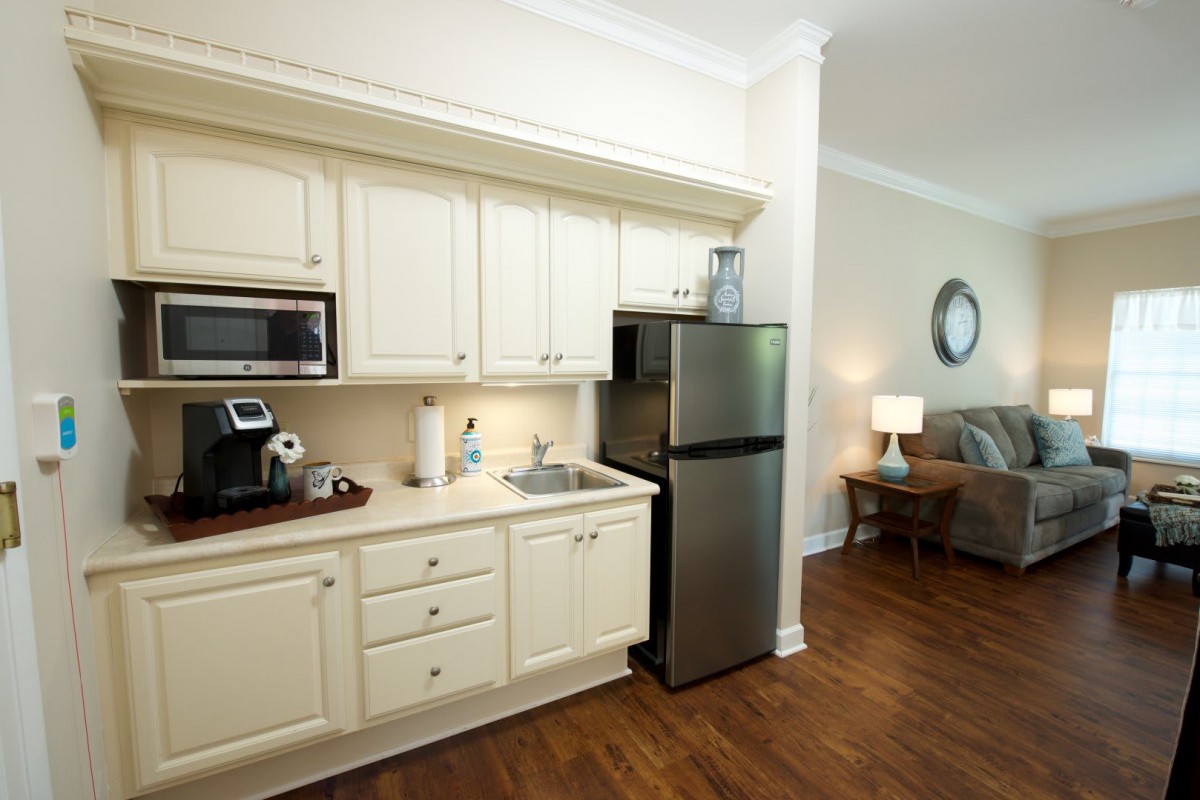 A cozy kitchenette with white cabinets, a stainless steel refrigerator, microwave, and coffee machine.