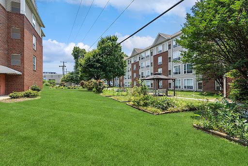 A serene residential landscape with well-maintained lawns and gardens, surrounded by apartment buildings under a clear blue sky.