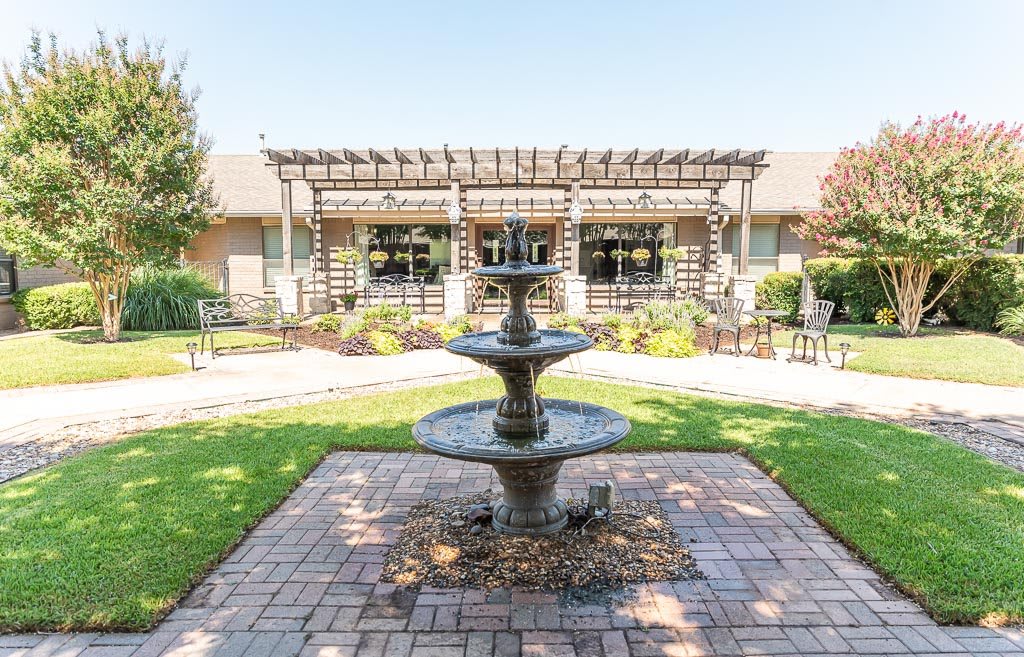 A picturesque courtyard with a central fountain and a surrounding garden featuring a pergola.