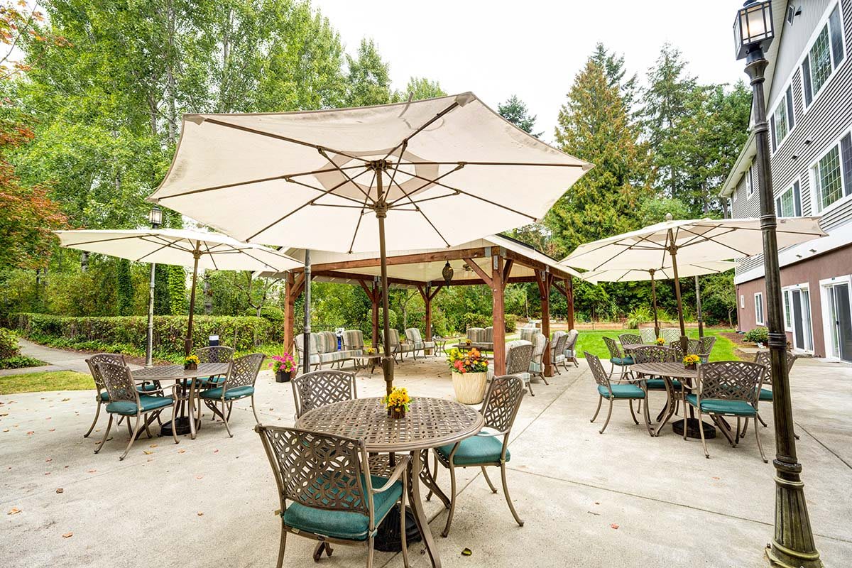 A serene outdoor patio area with tables, chairs, and umbrellas amidst lush greenery.