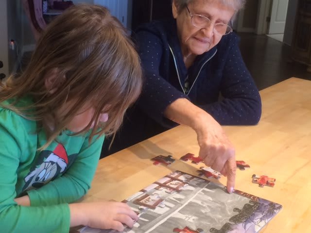 An elderly woman and a child working on a puzzle together at a table.