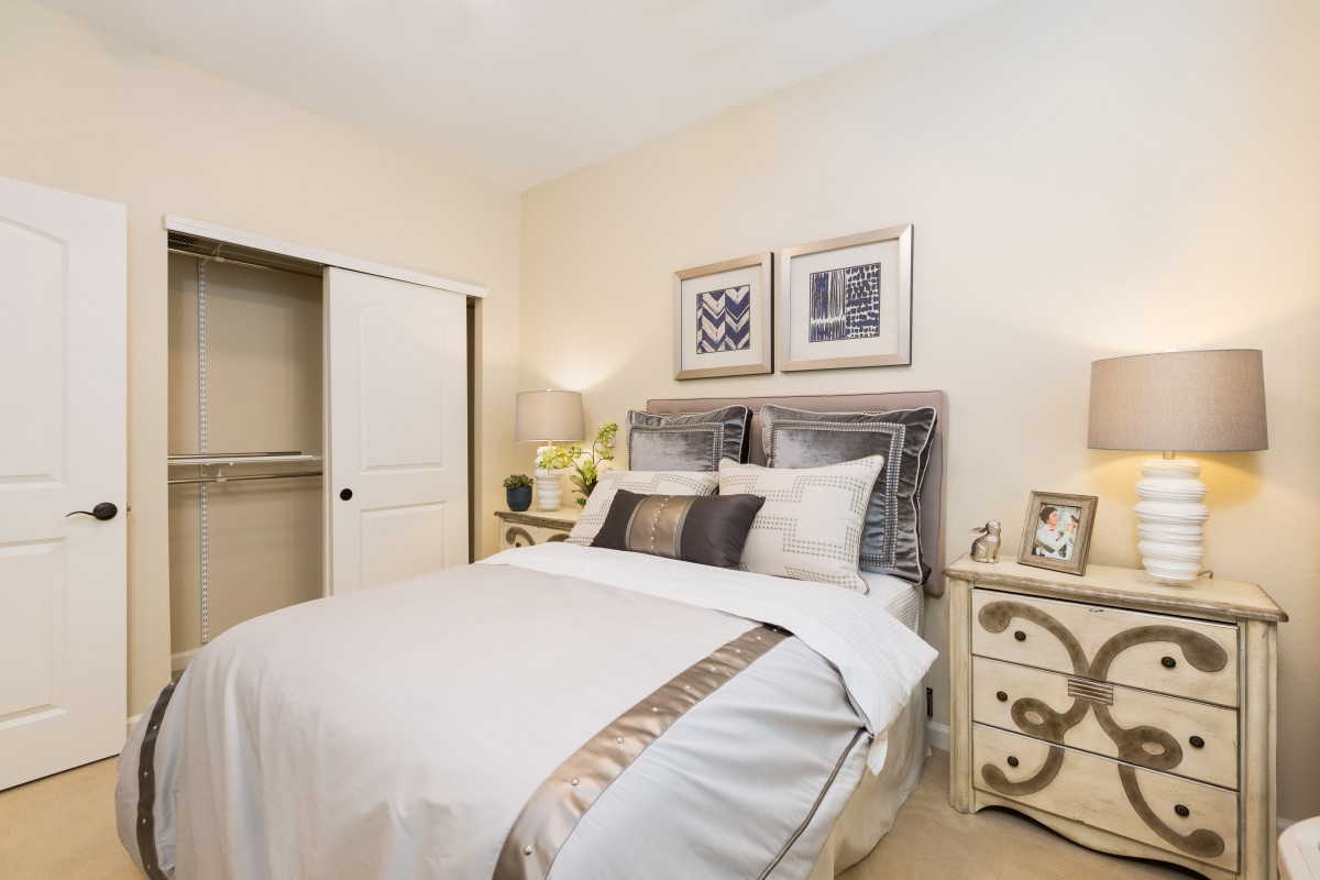 A cozy and elegantly furnished bedroom with a neatly made bed, decorative pillows, nightstands, and framed artwork on the wall.