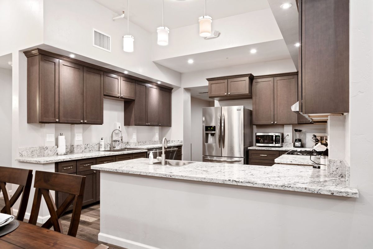 A modern kitchen featuring wooden cabinets, stainless steel appliances, and marble countertops with an island and pendant lighting.