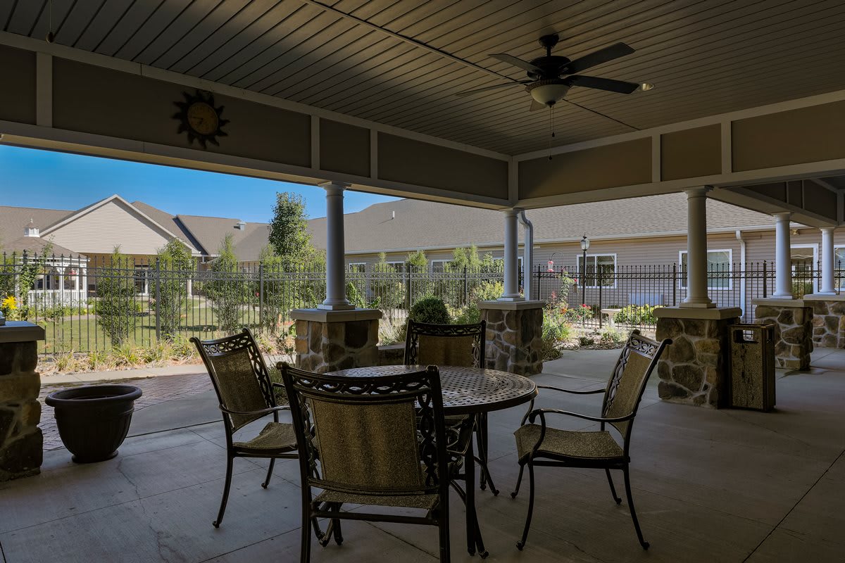 A covered patio with outdoor furniture, including a table and chairs, and a ceiling fan.
