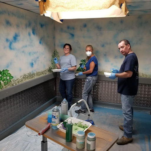 A group of three individuals working together to paint an artistic mural in a workshop.