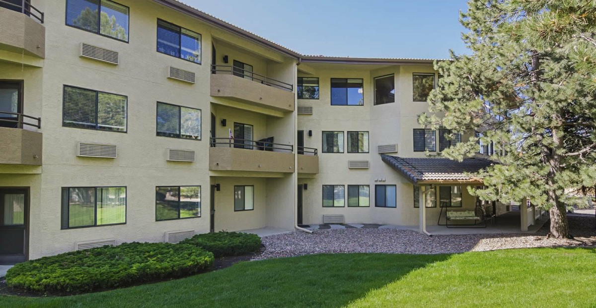 A multi-story apartment building with balconies, surrounded by a green lawn.