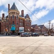 A historic brick building with a turret, located on an urban street with parked cars.
