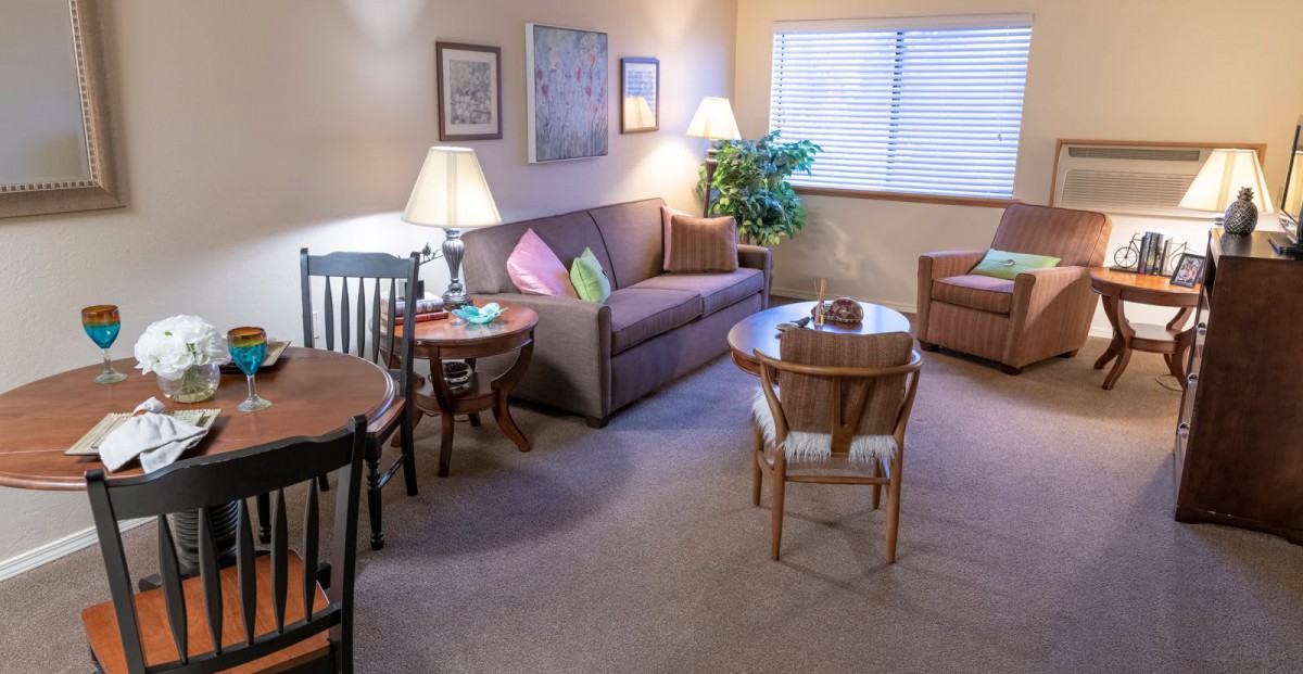 A cozy living room with a couch, chairs, and a table, illuminated by lamps.